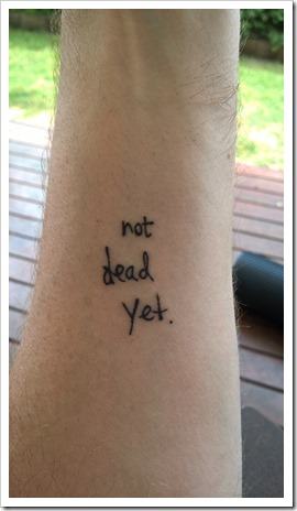 The words 'not dead yet' as a tattoo on an arm.